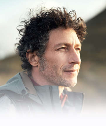 Hombre de cabello rizado, vistiendo una chaqueta azul, mirando hacia el horizonte.