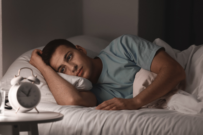 hombre joven tumbado de lado en la cama junto al despertador