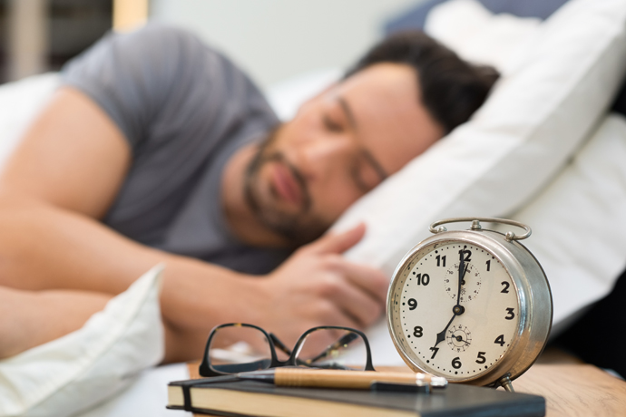 Hombre durmiendo con despertador en la mesa