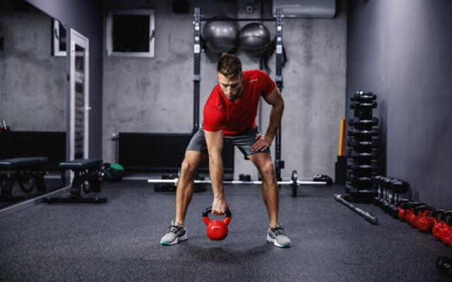 hombre levantando pesa kettlebell en gimnasio