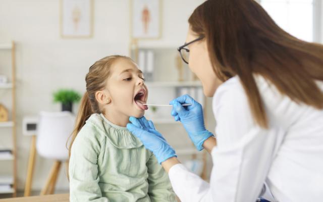 Doctora examinando si niña tiene pus en la garganta.