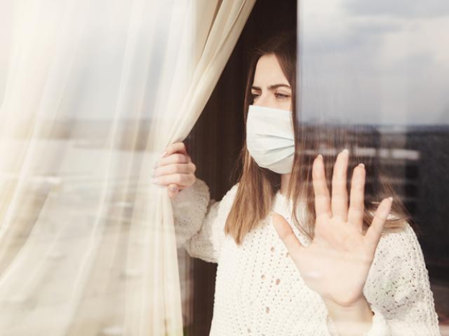 Mujer viendo desde su ventana con máscara