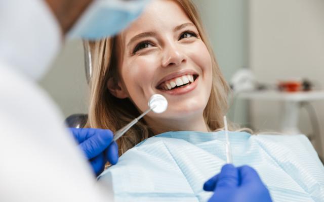 Dentista revisando si una mujer toma vitaminas para fortalecer sus dientes.